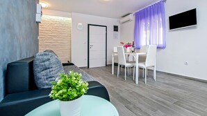 Un salon moderne comprenant un canapé, une petite table avec une plante, un coin repas avec des chaises, une horloge et un téléviseur fixé au mur.