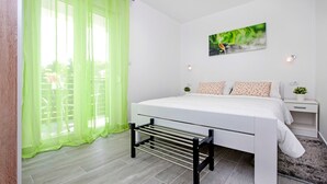 A modern bedroom with a bed, a nightstand, a small plant, and a window with sheer curtains.
