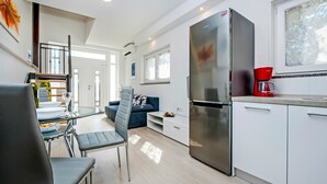 A modern kitchen with a stainless steel refrigerator, a red coffee maker, and a dining area with a glass table and chairs.