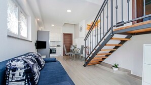 A modern living room with a blue sofa, a flat-screen TV, and a staircase leading to an upper level.