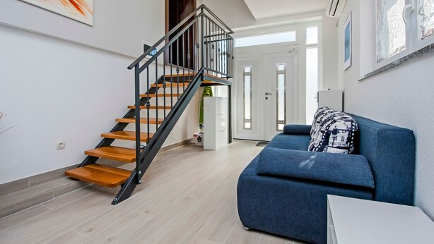 A modern living room with a wooden staircase, a blue sofa, and a white table.