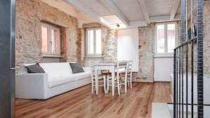 A cozy room with a white sofa, a dining table with chairs, and a stone wall. - CASA ROCCIA BIANCA - CIELO - Two Bedroom Apartment (Rovinj)