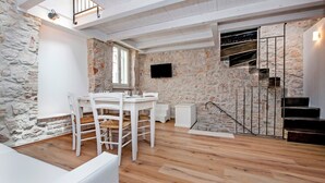 A modern interior with a stone wall, a wooden staircase, and a dining area with white furniture. - CASA ROCCIA BIANCA - CIELO - Two Bedroom Apartment (Rovinj)