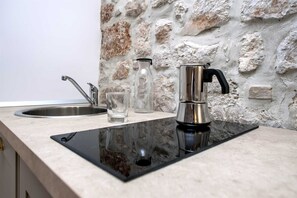 A kitchen with a black induction cooktop, stainless steel faucet, and a glass bottle. - CASA ROCCIA BIANCA - MARE - One Bedroom Apartment (Rovinj)