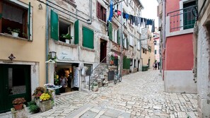 A narrow cobblestone street with buildings on either side, a shop named 'Atelier Heaven' with a visible entrance, and laundry hanging on a line.
