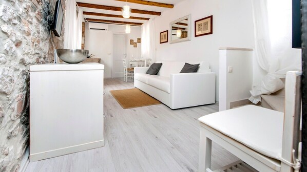 A modern living room with a white sofa, a dining table, and a kitchen area with a large bowl on a cabinet. - CA’ 3 VIE LAVANDA - One Bedroom Apartment (Rovinj)