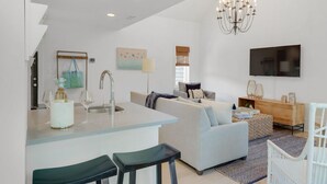 A modern kitchen with a central island, a dining area with bar stools, a living room with a sofa and a TV, and a chandelier. - PRIVATE BEACH/POOL ACCESS-Ultimate Getaway-Gulf Views-Steps to Beach-2 Bikes (Rosemary Beach)