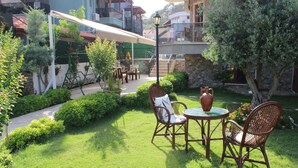 A patio with wicker furniture and a table, surrounded by greenery and a brick wall. - Iberia Villas (Ortaca)