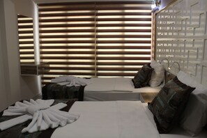 A hotel room with two beds, a large window with blinds, a decorative wall panel, and a bedside table with a lamp. - Iberia Villas (Ortaca)