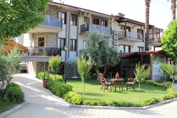 A multi-story hotel with balconies, a garden with chairs and a table, and a pathway leading to the entrance. - Iberia Villas (Ortaca)