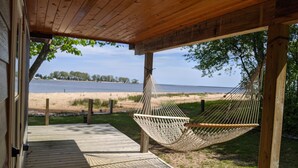 Ett trädäck med en hängmatta, utsikt över en strand och en vattenyta.