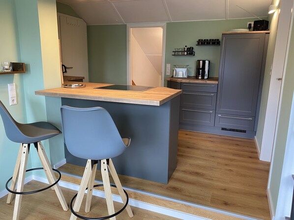 A compact kitchen with a central island, two bar stools, and a built-in refrigerator.