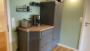 Una cocina compacta con tostadora integrada, cafetera y estantes para tazas y vasos.