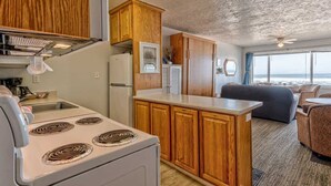 A compact kitchen with wooden cabinets, a white stove, and a small dining area with a sofa and table. - Sea Gypsy Rentals -  Oceanfront Suite - Pool! (Lincoln City)