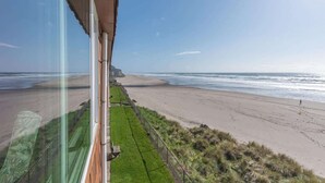 A beach view from a window overlooking a sandy beach with a grassy area and a fence. - Oceanfront Suite - Top Floor - Pool and Sauna - Sleeps 4! (Lincoln City)