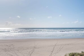Une plage où l’on voit des empreintes de pas menant à l’eau, un ciel dégagé et des vagues douces.