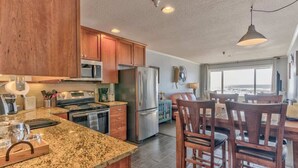 A modern kitchen with granite countertops, stainless steel appliances, wooden cabinets, and a dining area with a view. - Oceanfront Suite - Top Floor - Pool and Sauna - Sleeps 4! (Lincoln City)