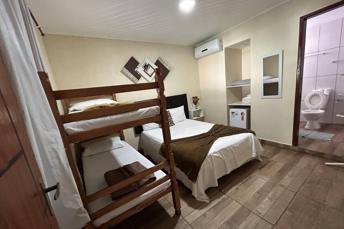 A room with bunk beds, a small desk, a mirror, a toilet, and an air conditioning unit.