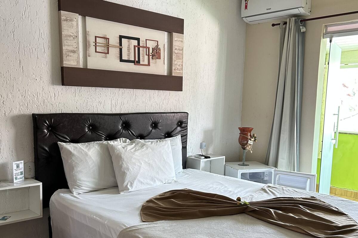 A neatly made bed with a brown throw blanket, a headboard with a decorative panel, and a wall-mounted air conditioner.