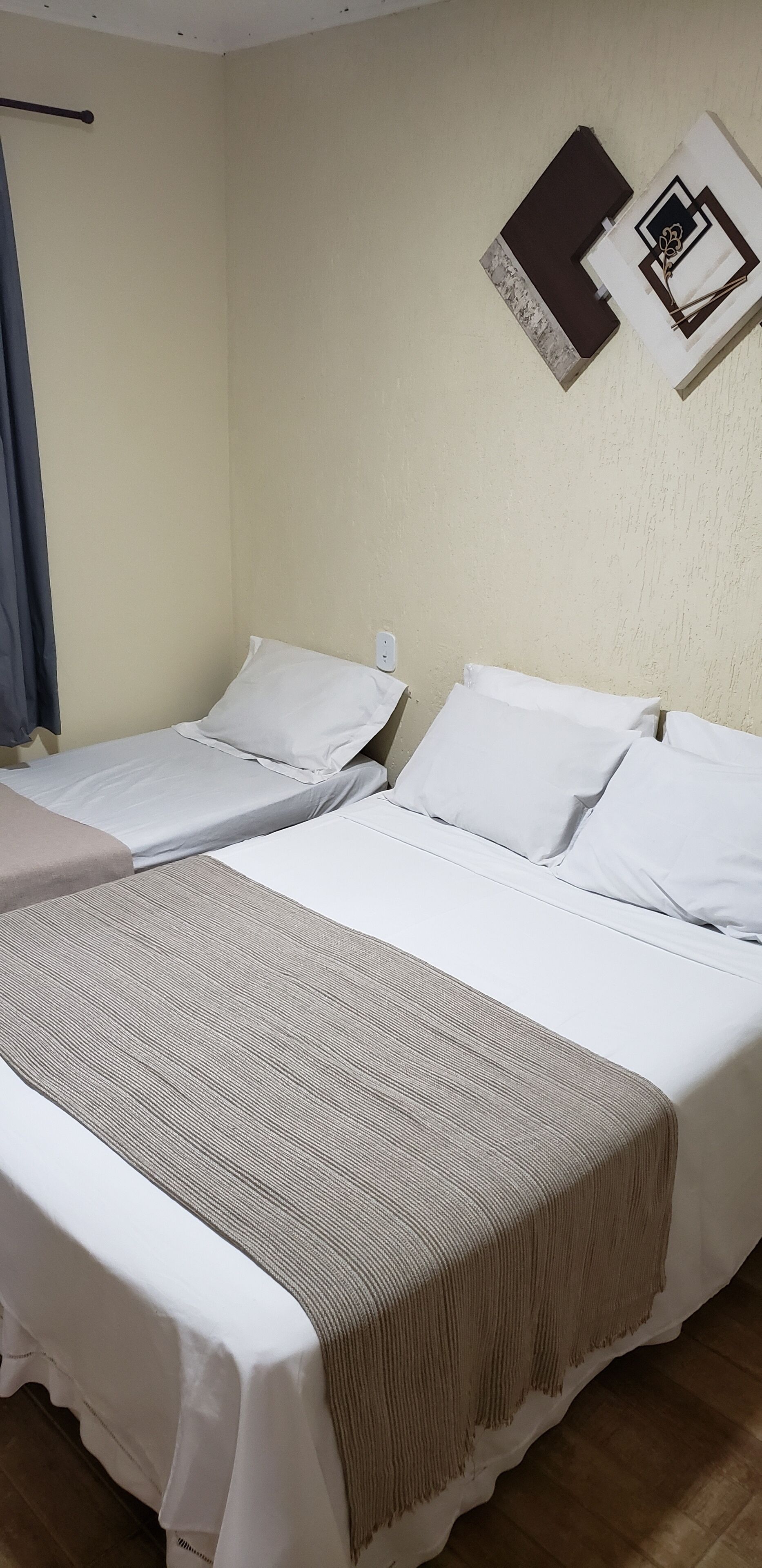 A hotel room with two single beds, a large bed with a beige blanket, and a wall-mounted artwork.