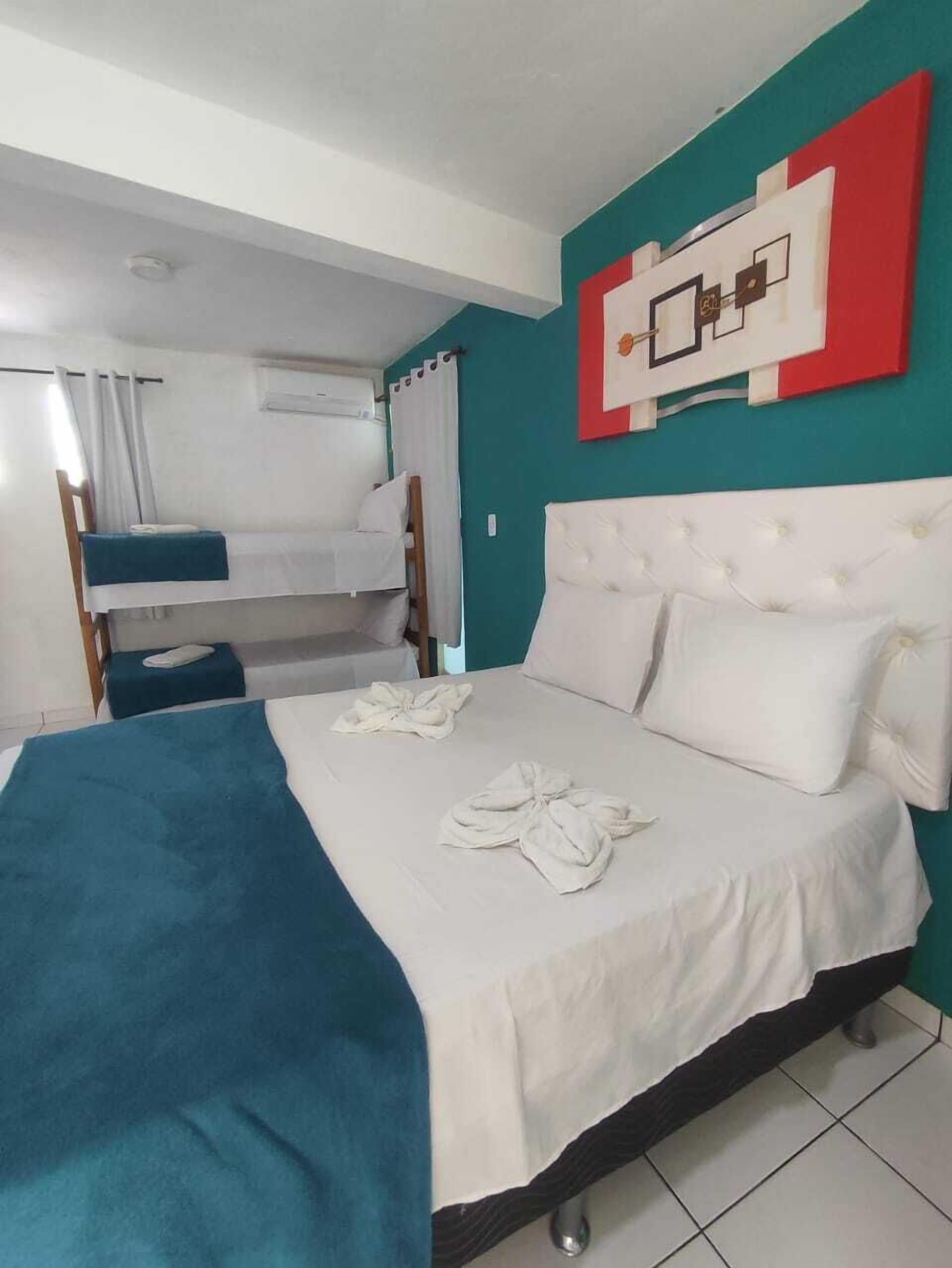 A hotel room with a bunk bed, a large bed with a white headboard, and a teal accent wall.