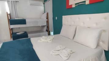 A hotel room with a bunk bed, a large bed with a white headboard, and a teal accent wall.