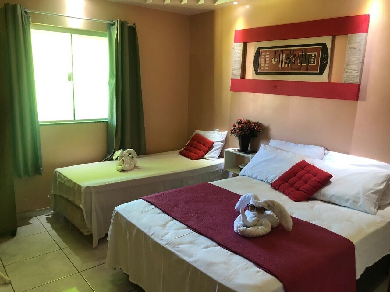 Habitación de hotel con dos camas, una ventana con cortinas, una obra de arte en la pared y una mesita con un jarrón de flores.