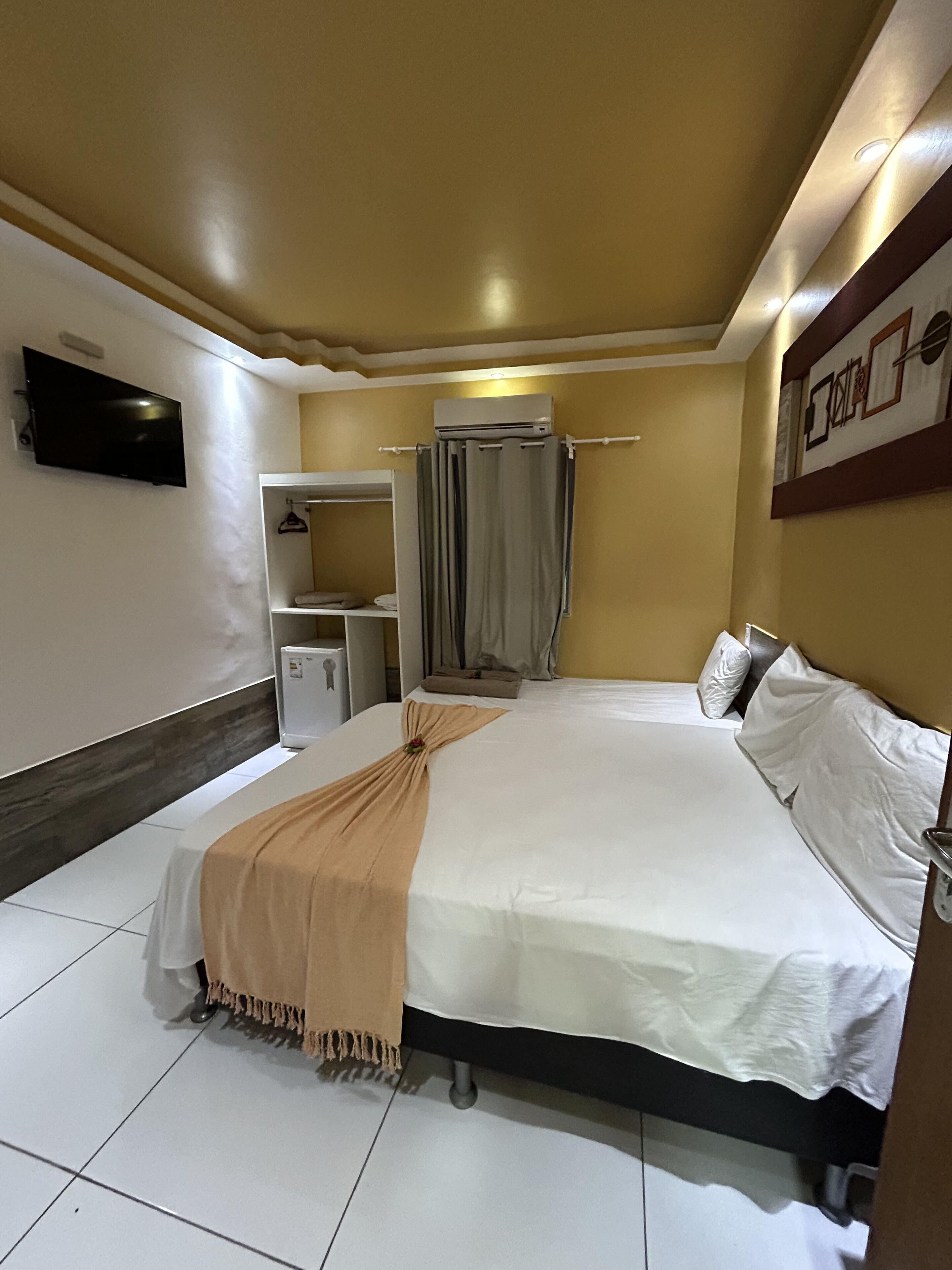 A hotel room with a bed, a television, a wardrobe, and a shower area.