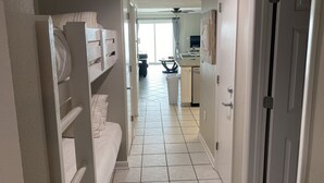 Un pasillo con una cama, un ventilador de techo y una cocina al fondo.