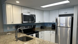 Una cocina moderna con armarios blancos, un refrigerador de acero inoxidable, un microondas, una estufa y un lavamanos.