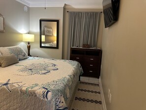 Een slaapkamer met een bed, een dressoir, een spiegel, een lamp en een raam met gordijnen.