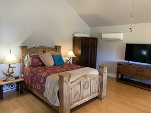 Une chambre à coucher avec un lit en bois, deux tables de chevet avec des lampes, une armoire, un téléviseur et un appareil de climatisation.