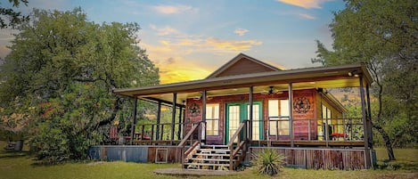 A wooden cabin with a porch, surrounded by trees and grass.