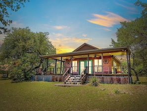 A wooden cabin with a porch, surrounded by trees and grass.