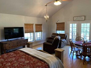 A spacious room with a large bed, a television, a leather recliner, a dining table with chairs, and a chandelier. - Hideout | Romantic Stay w/ Horses & Starry Skies (Pipe Creek)