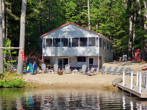 A two-story cabin with a dock extending into a lake, surrounded by trees.