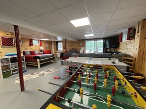 A cozy room with a foosball table, a bed, a sofa, and a TV.