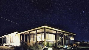 A modern house with a large open porch, a hammock, and a well-lit interior at night. - The Ridge at Joshua Tree (Joshua Tree)