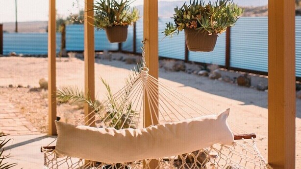 A hammock with a cushion, hanging from a wooden structure with a view of the sea and mountains in the background. - The Ridge at Joshua Tree (Joshua Tree)