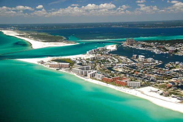 Stunning coastal resort with modern buildings, piers, and a bridge, situated along a white sandy beach and clear waters.