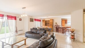 A spacious living room with a sofa, dining table, and kitchen area in the background. - GUIDEL BEACHES HOLIDAY HOME NEAR THE BEACHES (Guidel)