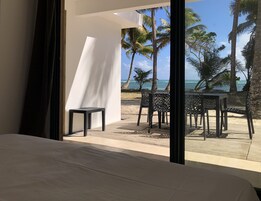 Una habitación con una cama grande, vistas a una playa con palmeras y una mesa y sillas afuera.