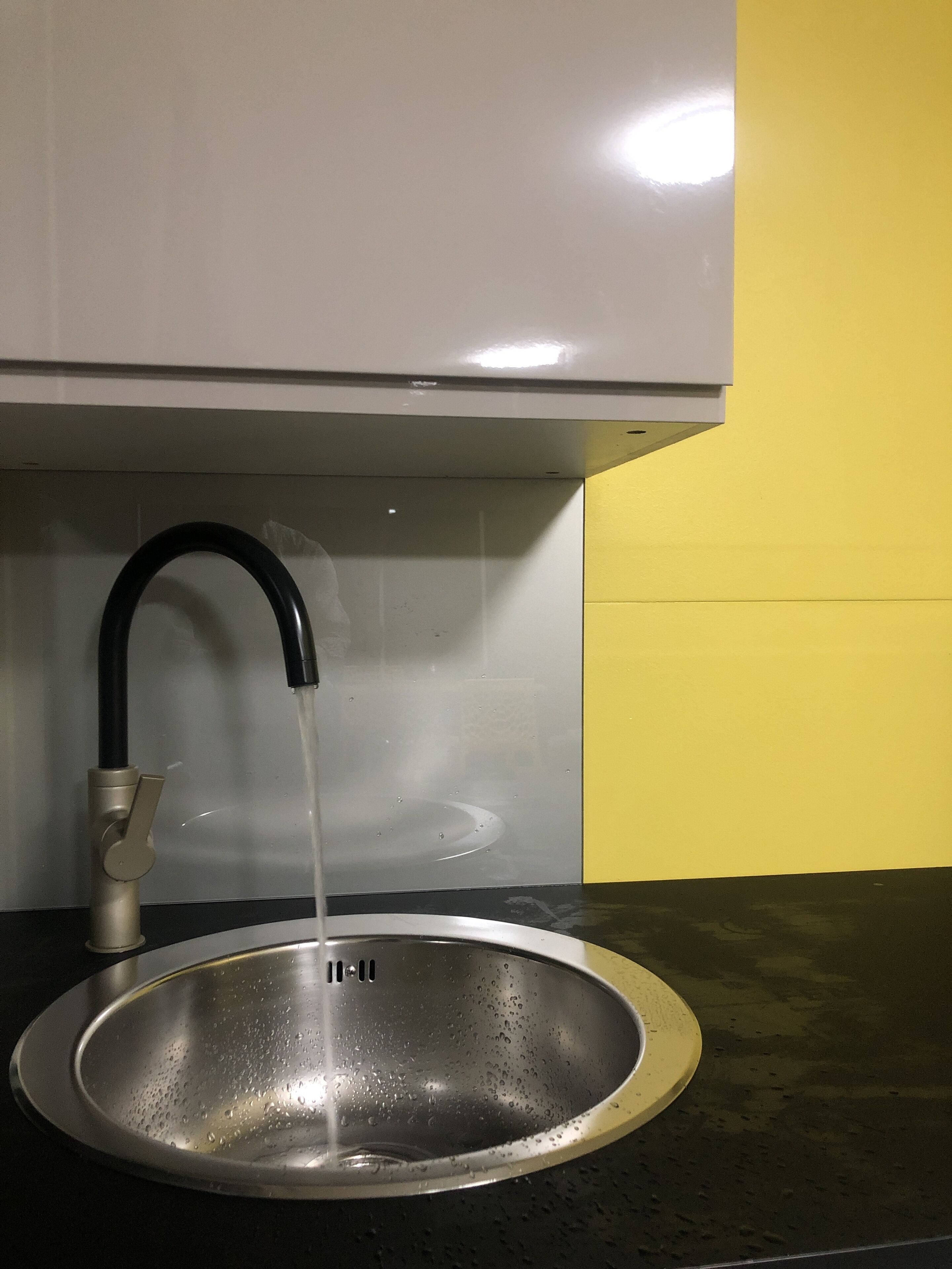 A stainless steel sink with a black faucet under a white cabinet, set against a yellow wall.