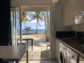 Una cocina con lavadora, una mesa y vistas a la playa con palmeras y el océano.