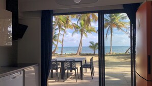 A room with a view of a beach, a dining table with chairs, and a ceiling fan. - Be On The Beach (Sainte-Anne)