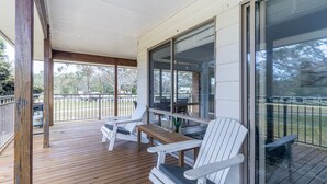 A covered outdoor seating area with wooden deck, white Adirondack chairs, and a table.