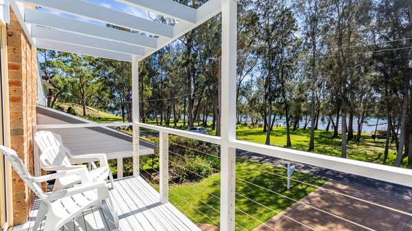 A covered outdoor area with white chairs and a view of a lake surrounded by trees. - Fair Views over the Inlet (Sussex Inlet)