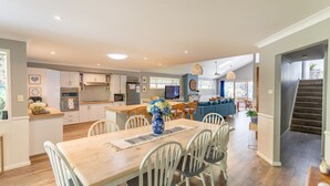 A spacious kitchen with modern appliances, a dining area with a wooden table and chairs, and a cozy living area with a sofa and decorative elements. - Fair Views over the Inlet (Sussex Inlet)