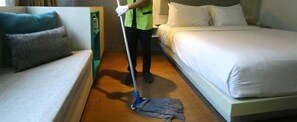 A hotel room with a bed, a sofa, and a person mopping the floor.