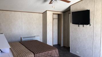 Una habitación de hotel con una cama, un ventilador de techo, un televisor montado en la pared y una puerta que da a otra habitación.